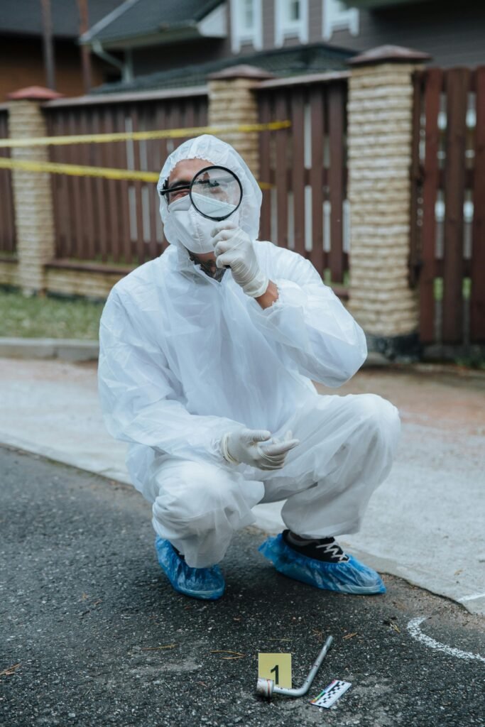 A forensic investigator in protective gear examines a crime scene with a magnifying glass.